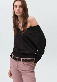 Czarny sweter off-shoulder dzianinowy z ryżowym splotem, zestawiony z jasnoróżowymi dżinsami i czarnym paskiem z złotymi ćwiekami.