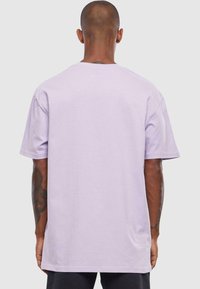 Lilla oversized T-shirt med korte ærmer, rund halsudskæring og en glat tekstur. Har en afslappet pasform og et enkelt design.