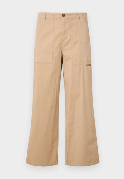 Pantalons cargo larges en coton beige avec des poches avant et un logo sur la poche arrière. Tissu léger avec une texture douce.