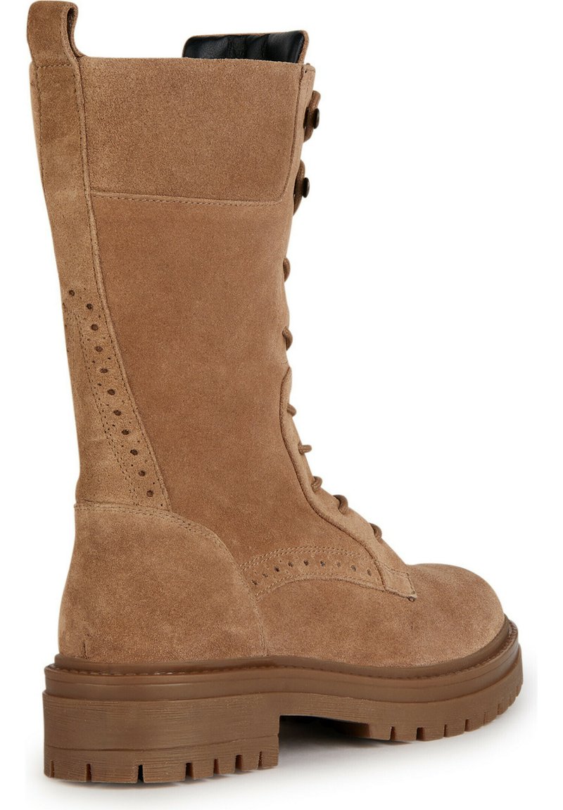 Tan suède laars tot halverwege het been met veters, dikke rubberen zool en decoratieve perforaties aan de zijkant en de hak, vanaf de buitenkant gezien.