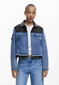 Cropped denim jacket with blue faded fabric and black leather accents, featuring a buttoned front, pockets, and frayed hem details.