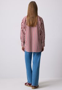 Camicia a righe con linee verticali bordeaux e crema, abbinata a jeans ampi blu chiaro. Calzature rosse con dettagli bianchi.