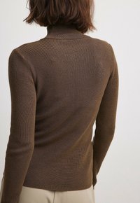 Ruskea ribbineulostettu pooloneule pitkillä hihoilla, vartalonmyötäinen malli ja pehmeä pinta, näkyvät sauman ompeleet selän puolella.