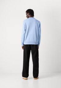 Sudadera azul claro de manga larga, con puños y dobladillo acanalados, combinada con pantalones de pierna ancha negros y zapatillas color crema.