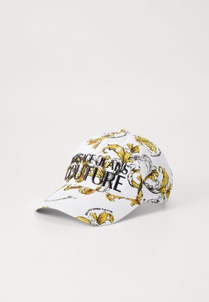 Gorra blanca con un patrón floral en amarillo y negro y el texto "Couture" prominentemente exhibido en la parte frontal. Material de algodón.