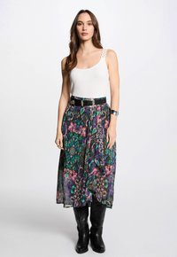 White tank top with lace straps, paired with a flowing, colorful patterned skirt featuring greens, purples, and floral designs. Black belt and boots.