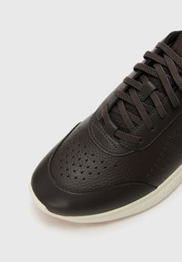 Mörkbruna sneakers med övre del i texturerat läder, perforerade detaljer och platta snörningar. Har en kontrasterande ljus gummisula.