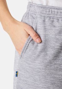Harmaat heather-joggerit, joissa on teksturoitu kangas, sivutasku ja pieni sininen ja keltainen lippuaksentti.