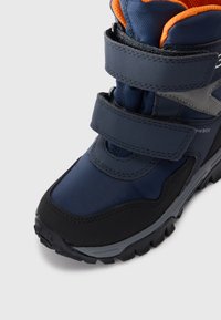 Mėlynos ir juodos žygio batų, turinčių sustiprintą pirštų apsaugą, Velcro dirželius, tekstūrinę medžiagą ir tvirtą gumos padą traukai.