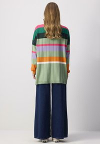Pull rayé coloré en vert, rose et orange, avec une texture côtelée. Assorti à un pantalon en denim bleu foncé à jambes larges et des baskets blanches.