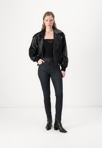 Veste bomber en cuir noir avec des revers larges, associée à un haut noir ajusté, un jean foncé taille haute et des bottines noires aiguilles.