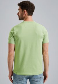Camiseta de manga corta verde claro con escote redondo y un pequeño parche en la parte trasera. Fabricada en suave algodón, combinada con jeans de mezclilla azul.