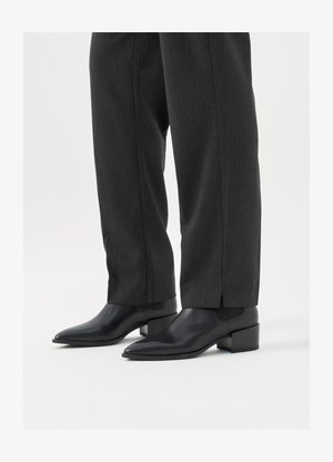 Schwarze Leder-Ankle-Boots mit spitzem Zehen und Blockabsatz, kombiniert mit grauen Nadelstreifenhosen. Glatte Textur, elegantes Design.