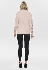 Light pink blazer with rolled sleeves and a straight cut, paired with black skinny jeans and high-heeled sandals. Smooth texture.