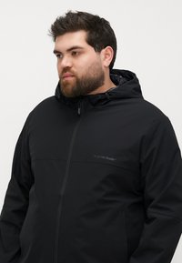 Black waterproof jacket with a hood, featuring a zippered front, smooth texture, and a subtle logo on the upper chest area.
