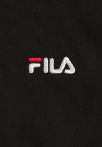 Svart tyg med en broderad logotyp i röda och vita trådar som stavar "FILA" i ett distinkt teckensnitt.
