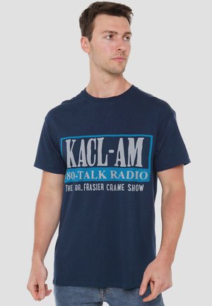 Dunkelblaues Baumwoll-T-Shirt mit einem auffälligen grafischen Druck, der den Text "KACL-AM 80-TALK RADIO" und "DIE DR. FRASIER CRANE SHOW" in kontrastierenden Farben zeigt.