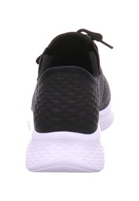 Baskets de sport noires avec une tige en mesh texturé, un talon noir lisse et une semelle en caoutchouc blanc au motif en vagues.