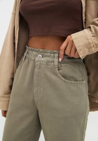 Pantalon à taille élastique couleur vert olive avec une fermeture à bouton, doté de poches latérales et d'une texture lisse, associé à un top court côtelé marron.