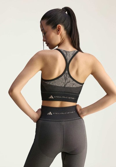Black sports bra with textured design, featuring a racerback and logo. High-waisted leggings in matching black with subtle ribbing and logo detail.