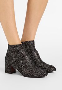 Botas de tobillo texturizadas en blanco y negro con punta ligeramente afilada y tacón cuadrado, que presentan una correa decorativa con un acento de hebilla plateada.