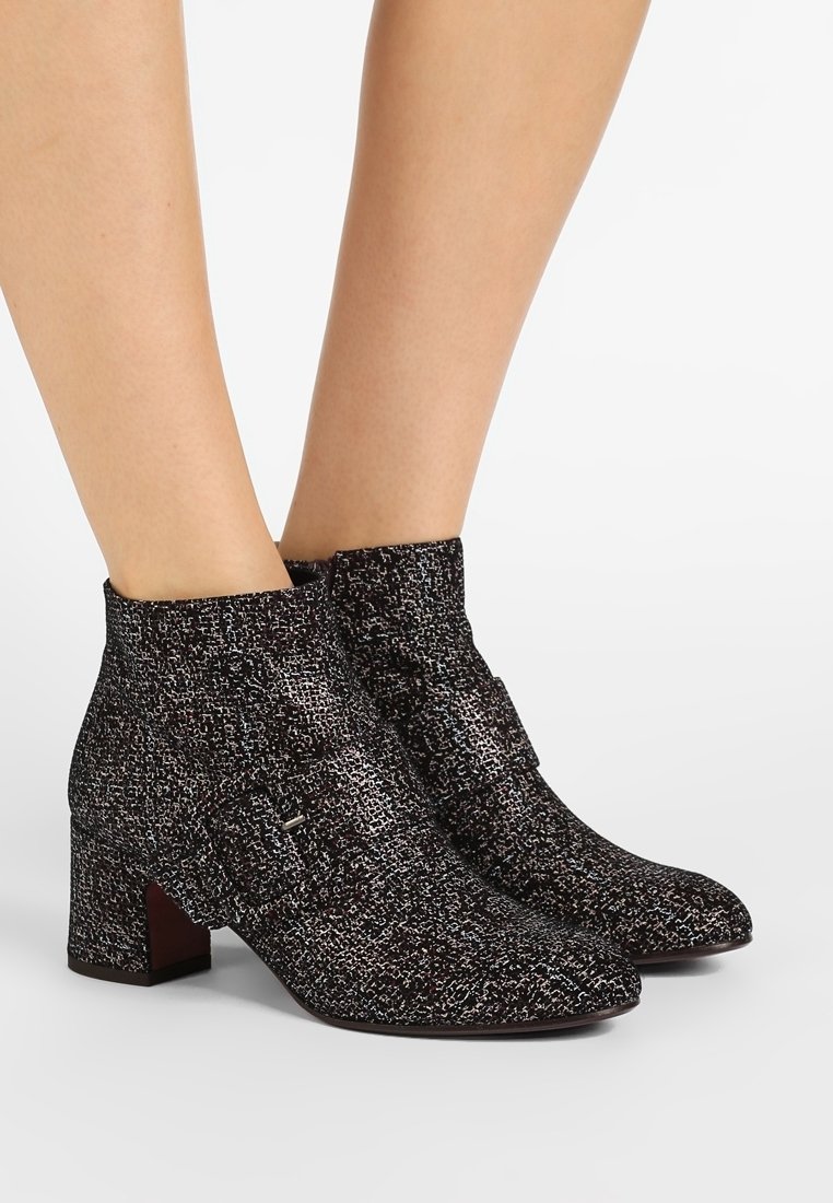 Botas de tobillo texturizadas en blanco y negro con punta ligeramente afilada y tacón cuadrado, que presentan una correa decorativa con un acento de hebilla plateada.