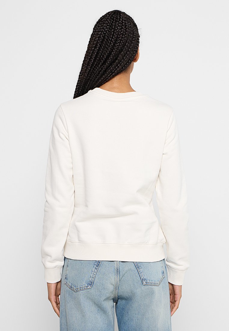 Felpa bianca in cotone con scollatura rotonda, polsini e orlo a costine, e una vestibilità comoda, abbinata a jeans chiari a vita alta.