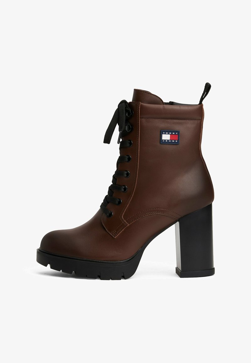 Botín de cuero marrón hasta el tobillo con punta redonda, tacón grueso negro, parte delantera con cordones y parche de marca. Presenta un acabado texturizado y suela resistente.