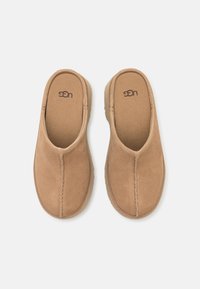 Scarpe slip-on in suede beige con soletta imbottita, caratterizzate da cuciture visibili lungo i bordi e una punta rotonda.