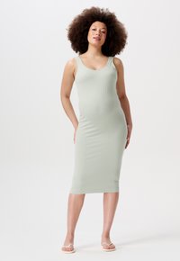Robe midi en vert menthe à côtes, avec des bretelles larges, une coupe ajustée et une texture lisse, portée avec des sandales blanches plates.