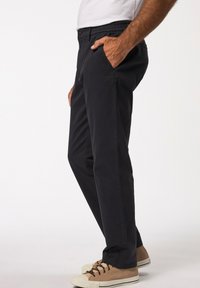 Granatowe spodnie slim-fit wykonane z lekkiego materiału, z bocznymi kieszeniami i elastycznym pasem, zestawione z beżowymi trampkami z płótna.