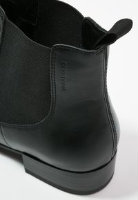 Botín negro con cuero liso y paneles elásticos, puntera redonda, tacón bajo apilado y una lengüeta en la parte trasera para ponerlo con facilidad.