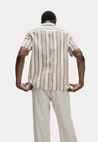Korte mouwen gestreept shirt in beige en wit met blauwe accenten. Zachte textuur, relaxte pasvorm en vierkante zoom. Gepaard met lichtgekleurde broeken.