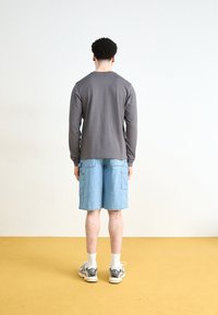 Gray long-sleeve shirt paired with blue denim shorts. The shorts feature side pockets. White socks and athletic shoes are worn.
