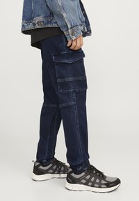 Pantalones cargo azul oscuro con múltiples bolsillos, con un diseño ajustado y puños elásticos. Combinados con zapatillas deportivas negras y grises.