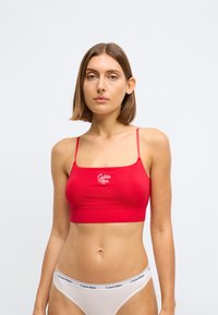 Rode cropped bralette gemaakt van gladde stof met verstelbare banden en een logo op de voorkant. Gecombineerd met lichtgekleurde onderkleding met branding.