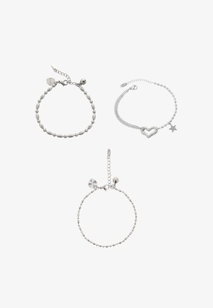 Drie zilveren armbanden: één met ovale kralen, één met een hart- en sterbedel, en een derde met ronde kralen en een klein label.