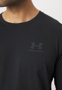 Schwarzes, langärmliges T-Shirt aus glattem Stoff mit rundem Ausschnitt. Verfügt über ein dezentes, dunkelgraues Under Armour-Logo auf der Brust.