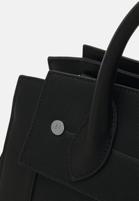 Czarna skórzana torebka o teksturowanej powierzchni, z podwójnymi uchwytami i metalowym logo na przedniej klapie.