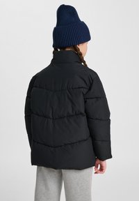 Svart puffjacka med hög krage, med diagonala quiltade sektioner. Sammanvävd med en mörkblå stickad mössa, med textur och ribbor.
