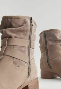Bottines en cuir tan avec une tige en daim doux, fermeture éclair sur le côté et sangles superposées. Le talon a une texture en bois marron.