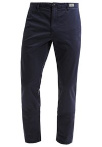 Pantalon slim fit bleu marine pour homme avec passants de ceinture, fermeture avant par bouton et zip, et une petite étiquette logo en tissu sur la ceinture.