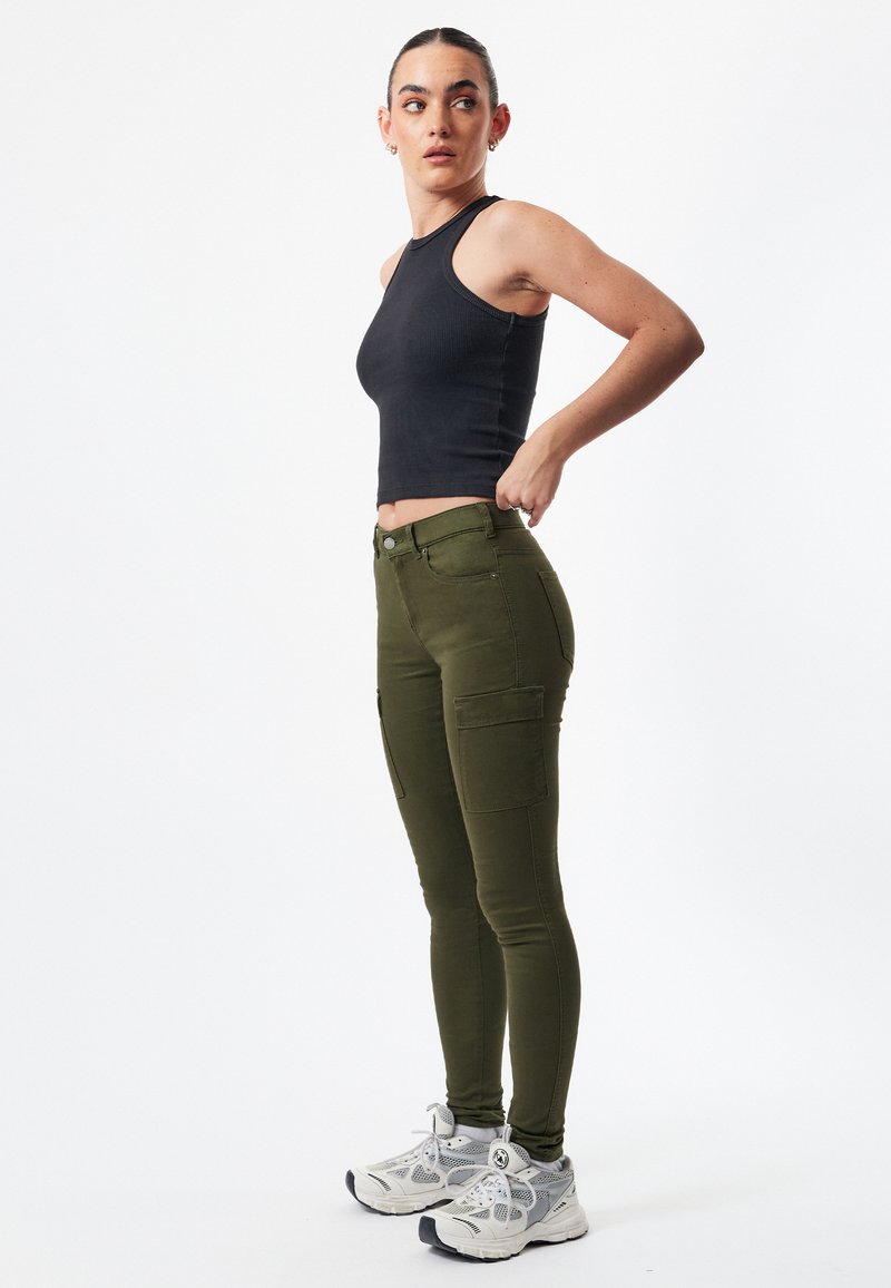 Pantalones cargo color verde oliva con bolsillos laterales, combinados con una camiseta sin mangas negra y zapatillas gris-blancas con detalles de malla.