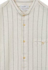 Camicia beige chiaro con righe verticali nere, colletto alla cinese, chiusura frontale con bottoni e tasca. Realizzata in tessuto testurizzato. Vestibilità regolare.