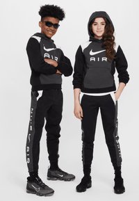 Black and grey Nike activewear set featuring hooded sweatshirts and joggers, with logo accents and contrasting panels. Textured sneakers.