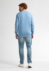 Lichtblauwe gebreide trui met ribbels aan de mouwen en zoom, gecombineerd met vervaagde blauwe jeans en beige sneakers, gezien vanuit de achterkant.