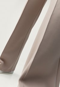 Kalhoty s širokými nohavicemi v dvoubarevném provedení s hladkou, elastickou látkou. Barvy zahrnují světle hnědou a taupe s jemnými švy.