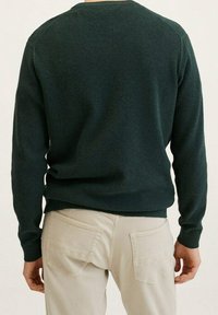 Ciemnozielony, teksturowany sweter z okrągłym dekoltem, długimi rękawami raglanowymi i prążkowanymi mankietami, zestawiony z jasnymi spodniami.