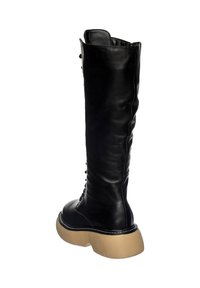 Stivale alto in pelle nera con punta arrotondata, suola chunky beige e dettagli in pizzo lungo il lato. Texture liscia in tutto.
