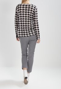 Haut à manches longues à motif pied-de-poule noir et blanc associé à un pantalon à carreaux. Le mannequin porte des bottines blanches à talon rond.